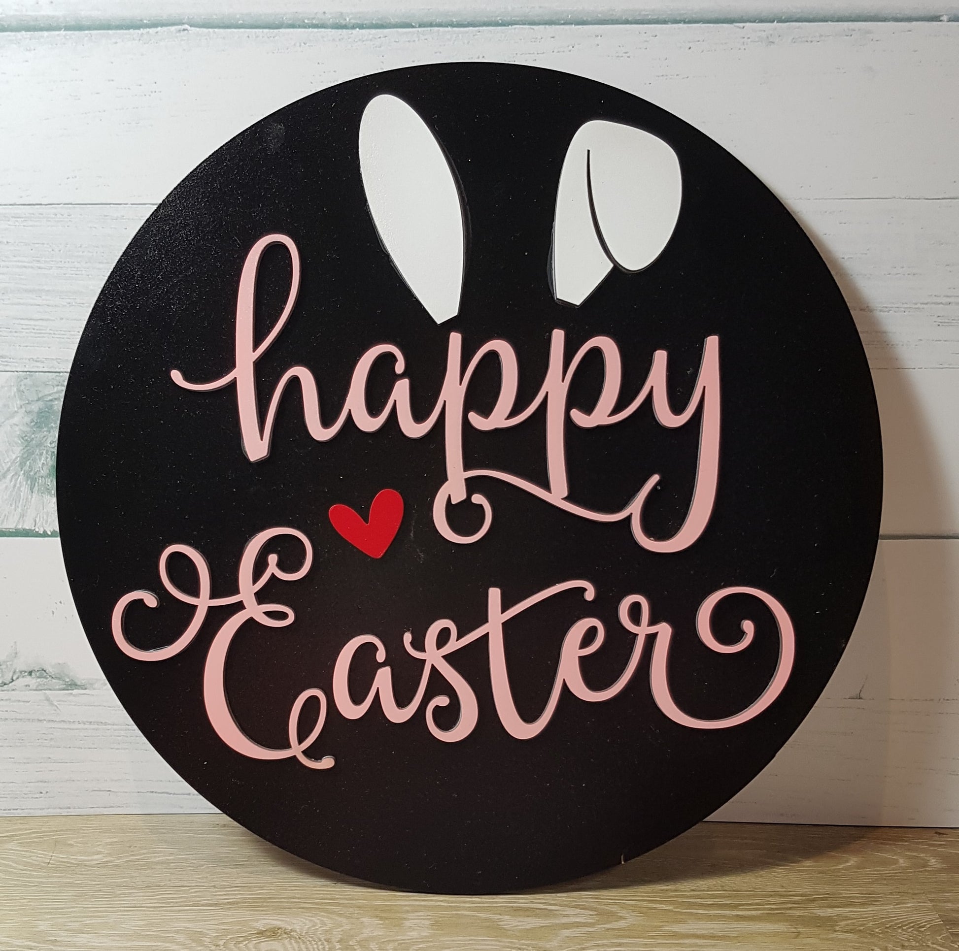 Elevate your Easter decor with our charming round Happy Easter sign. Available in three background colors and adorned with white bunny ears and a red heart, this 26cm x 26cm sign adds a festive touch to any space.