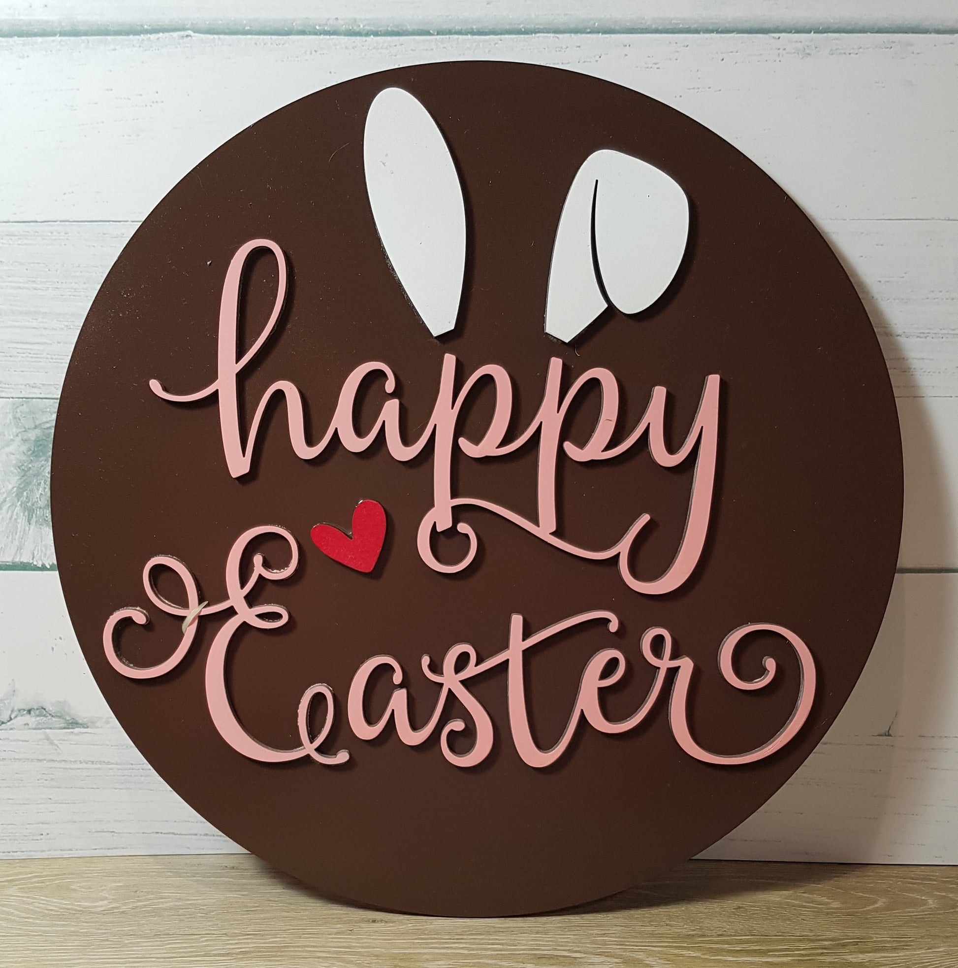 Elevate your Easter decor with our charming round Happy Easter sign. Available in three background colors and adorned with white bunny ears and a red heart, this 26cm x 26cm sign adds a festive touch to any space.