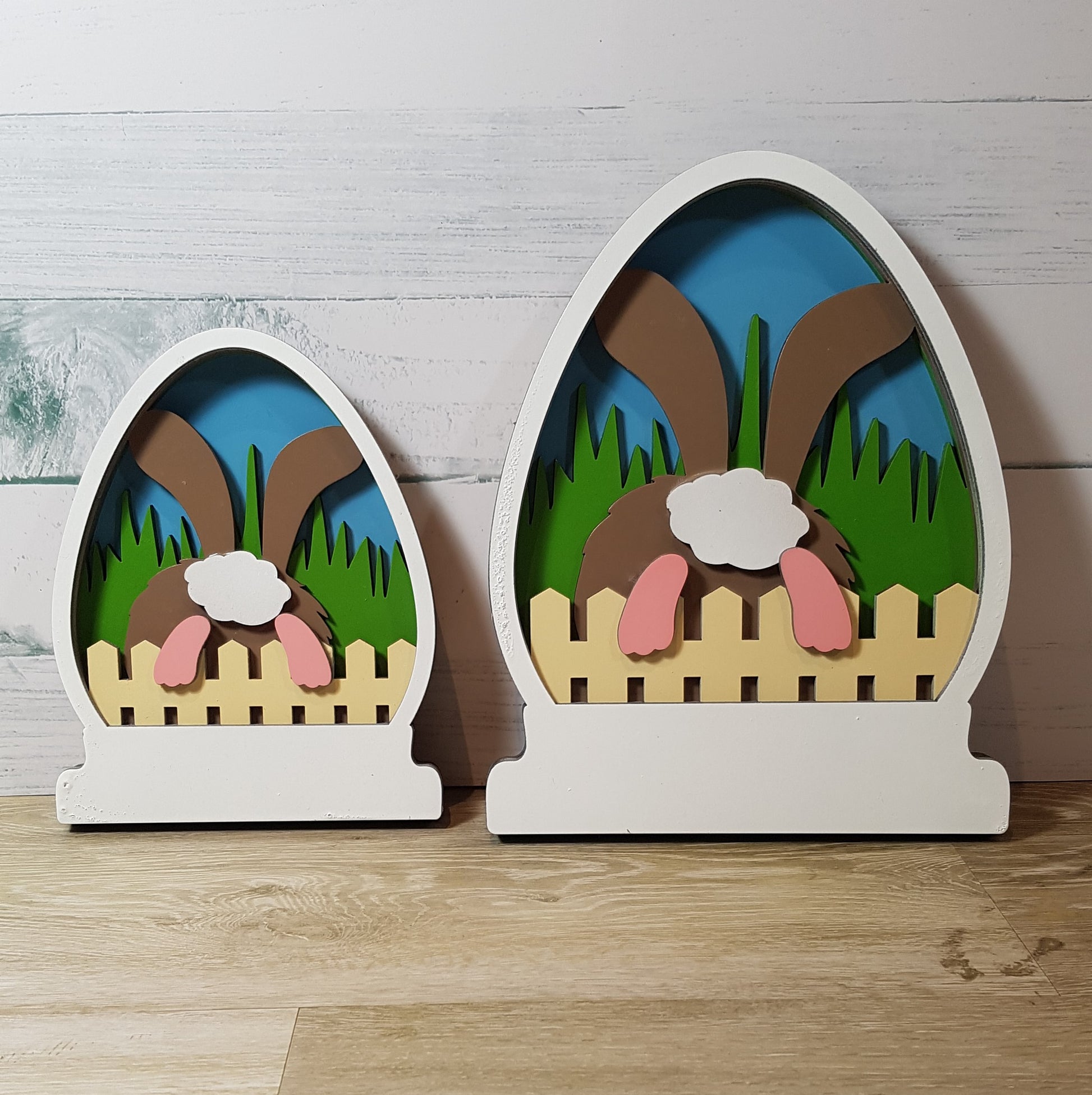 Explore our Easter-themed 5-layered CO2 laser-cut signs: charming egg shapes, available in Large (15.7cm x 20cm) or Small (12cm x 15cm). Adorable bunny hops over rustic fence into serene garden scene against blue sky backdrop. Meticulously crafted from high-quality materials. Perfect for Easter decor enthusiasts. Celebrate Easter joy with Turtle and Wolf Makers and Crafters.