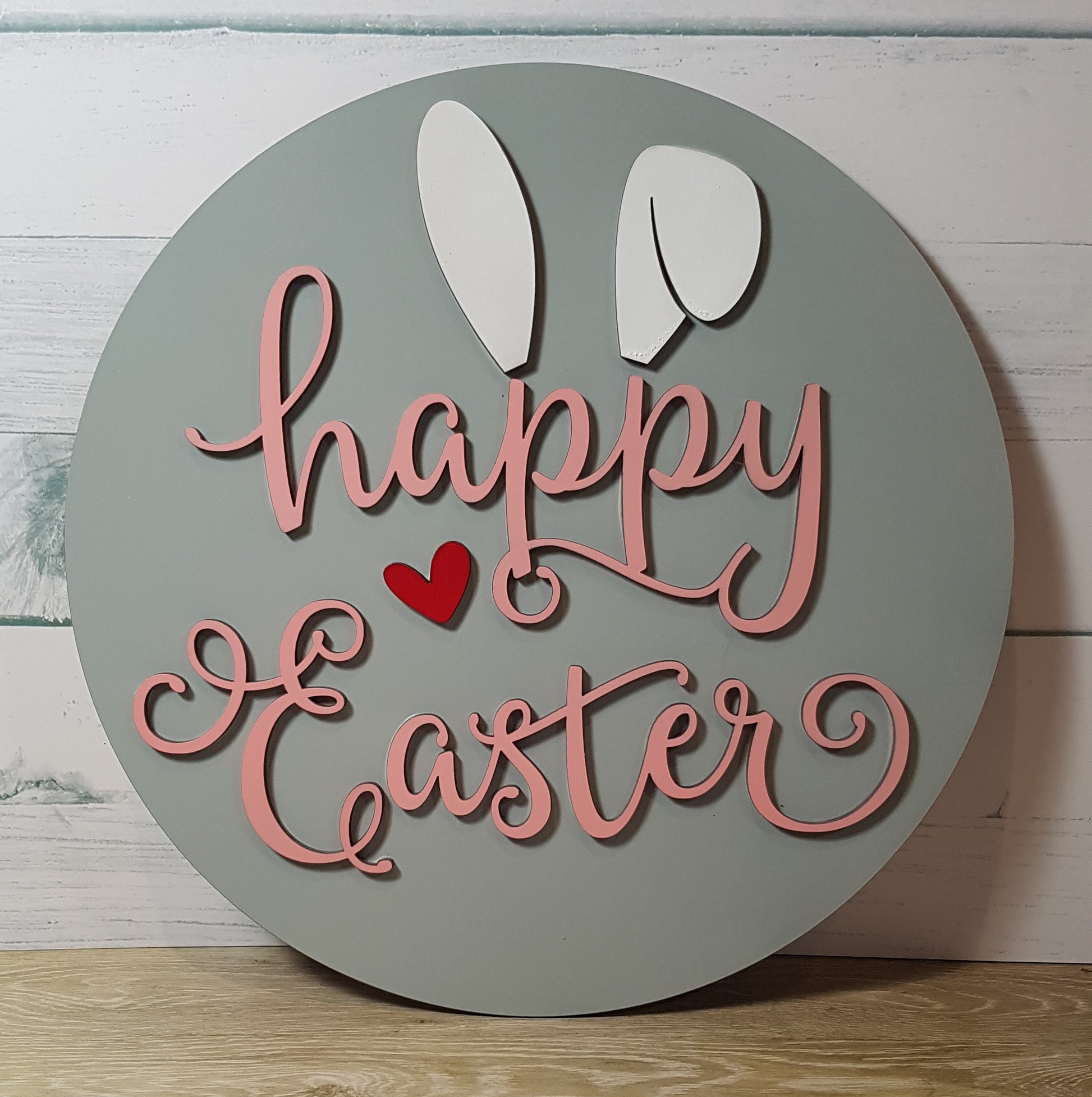 Elevate your Easter decor with our charming round Happy Easter sign. Available in three background colors and adorned with white bunny ears and a red heart, this 26cm x 26cm sign adds a festive touch to any space.